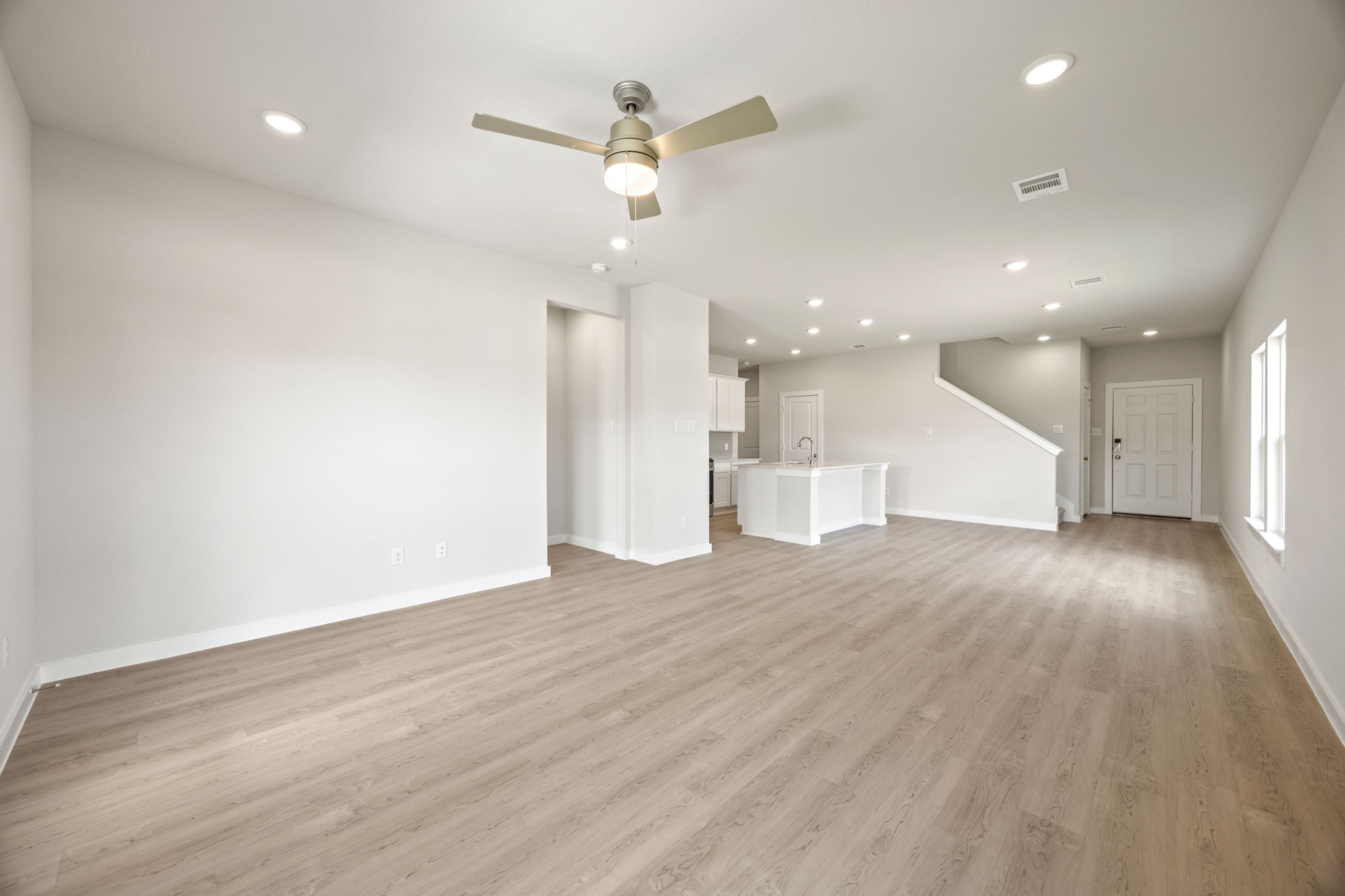 A large empty room with a ceiling fan and a wood floor.