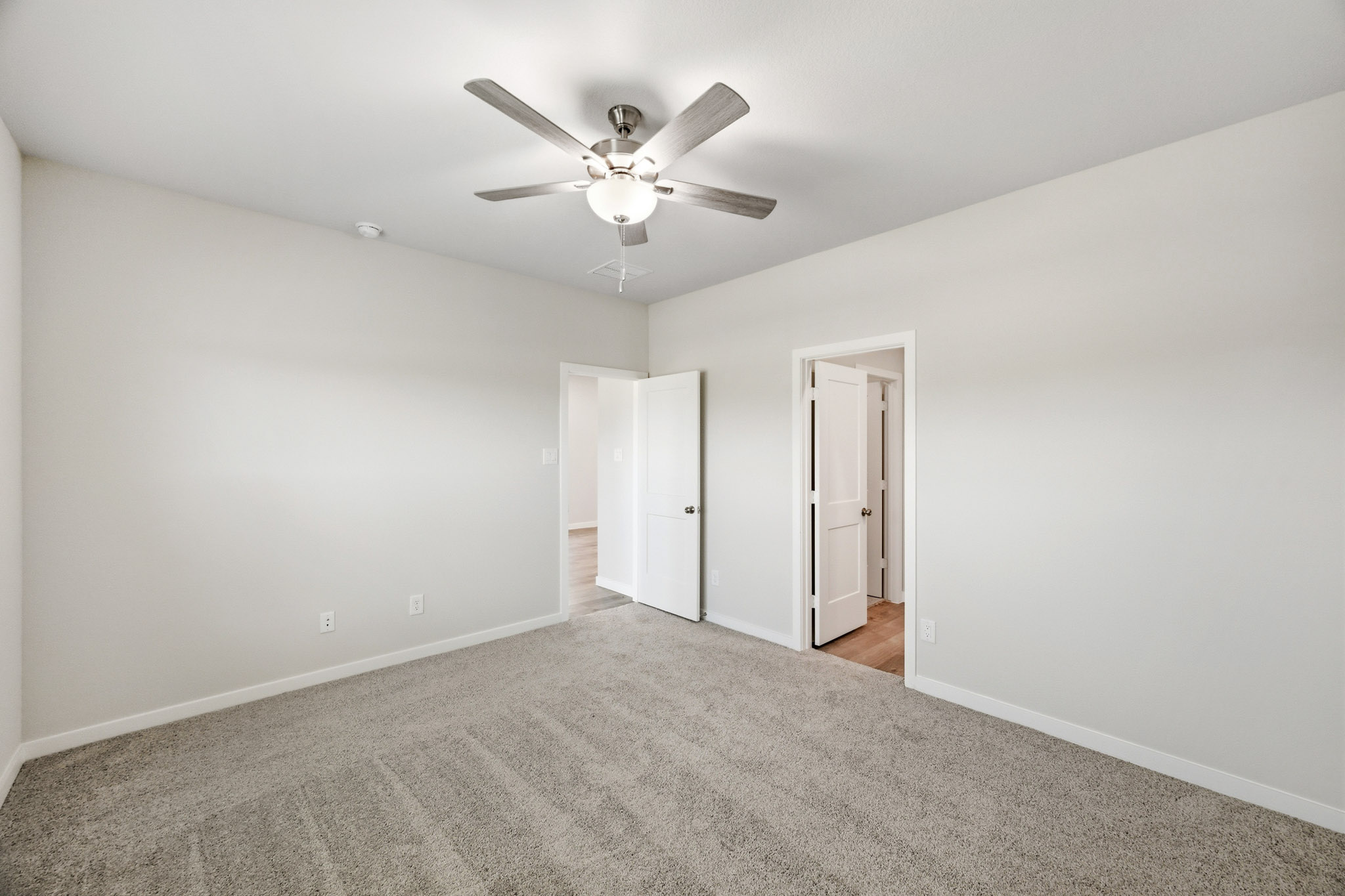 A room with a ceiling fan and a carpet.